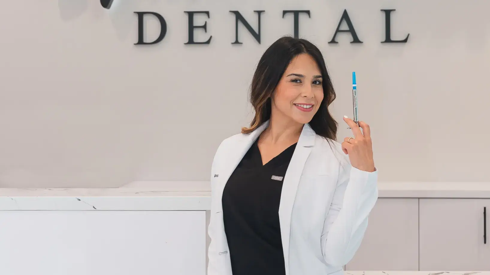 A woman holding a toothbrush in front of a dental sign.