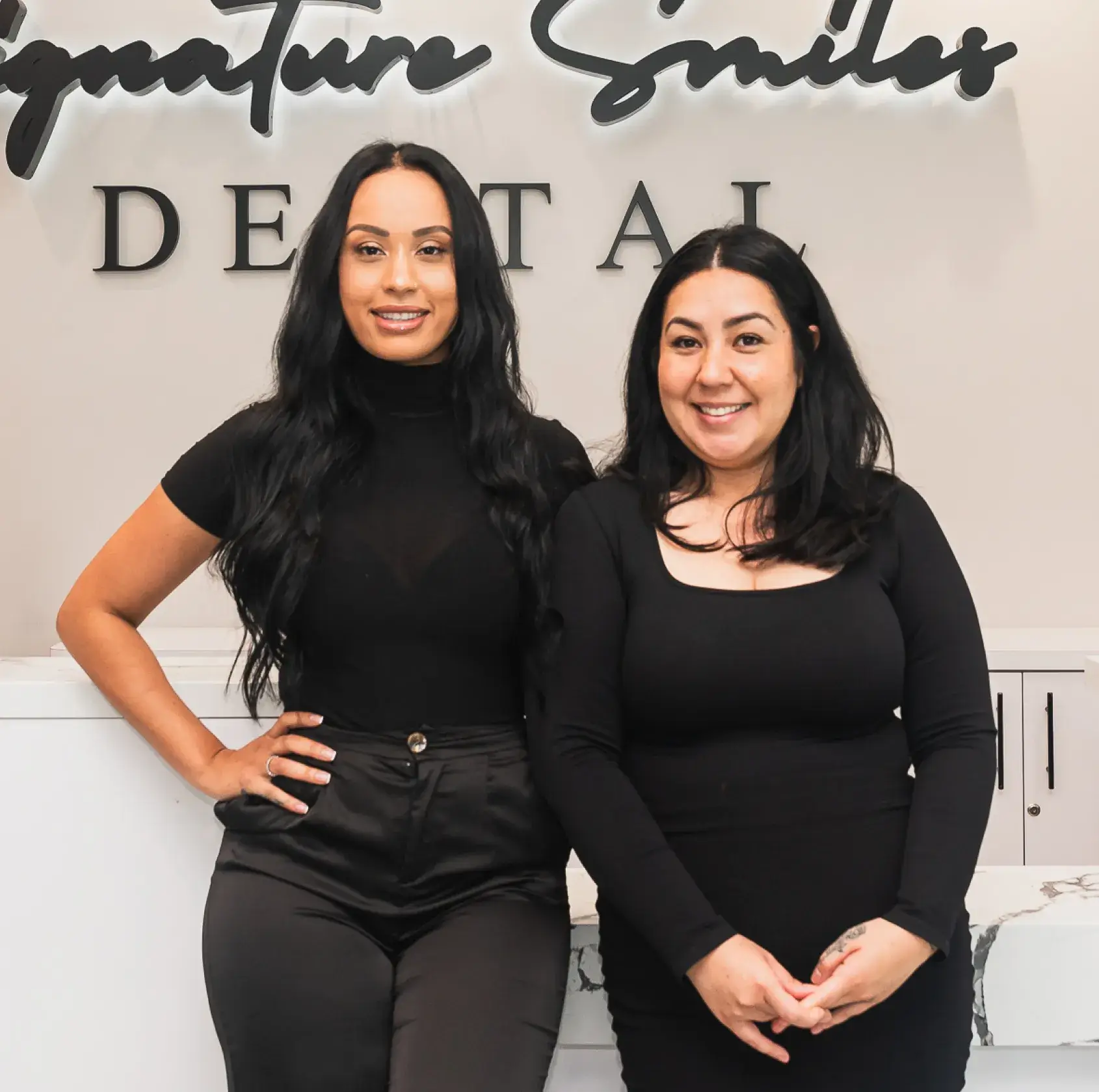 Two women standing next to each other in front of a sign.