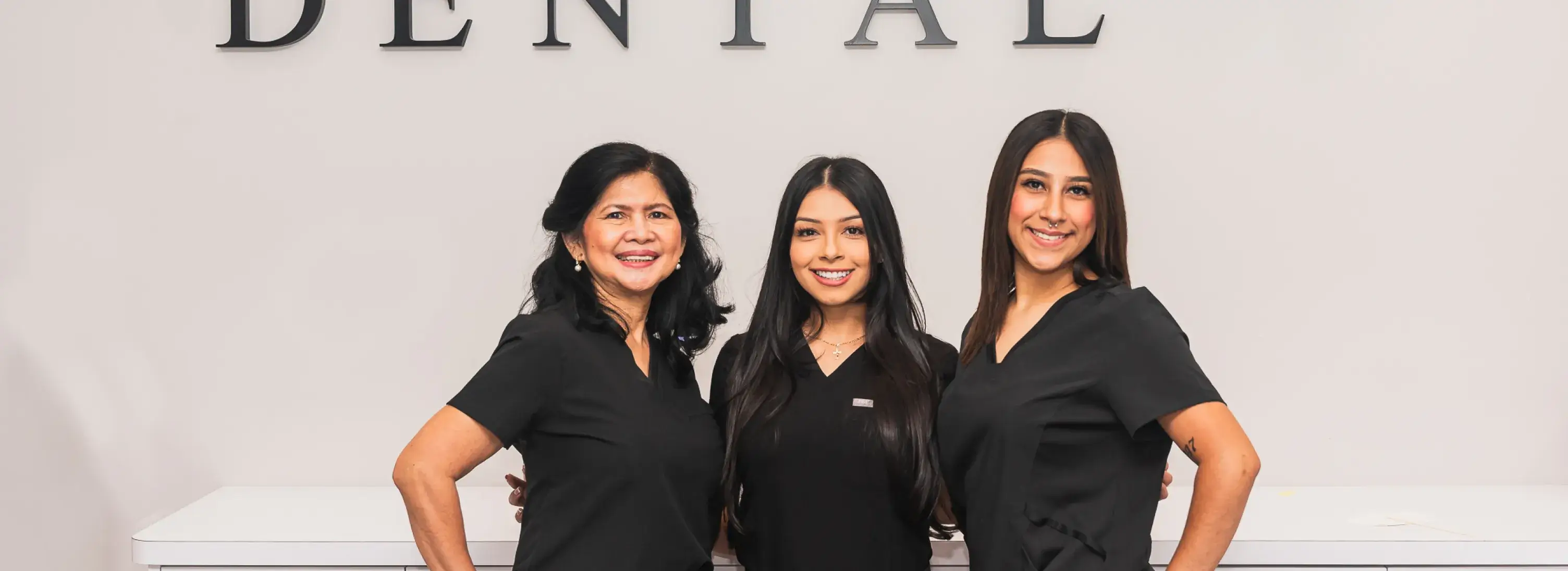 Three women standing next to each other in front of a dental sign.