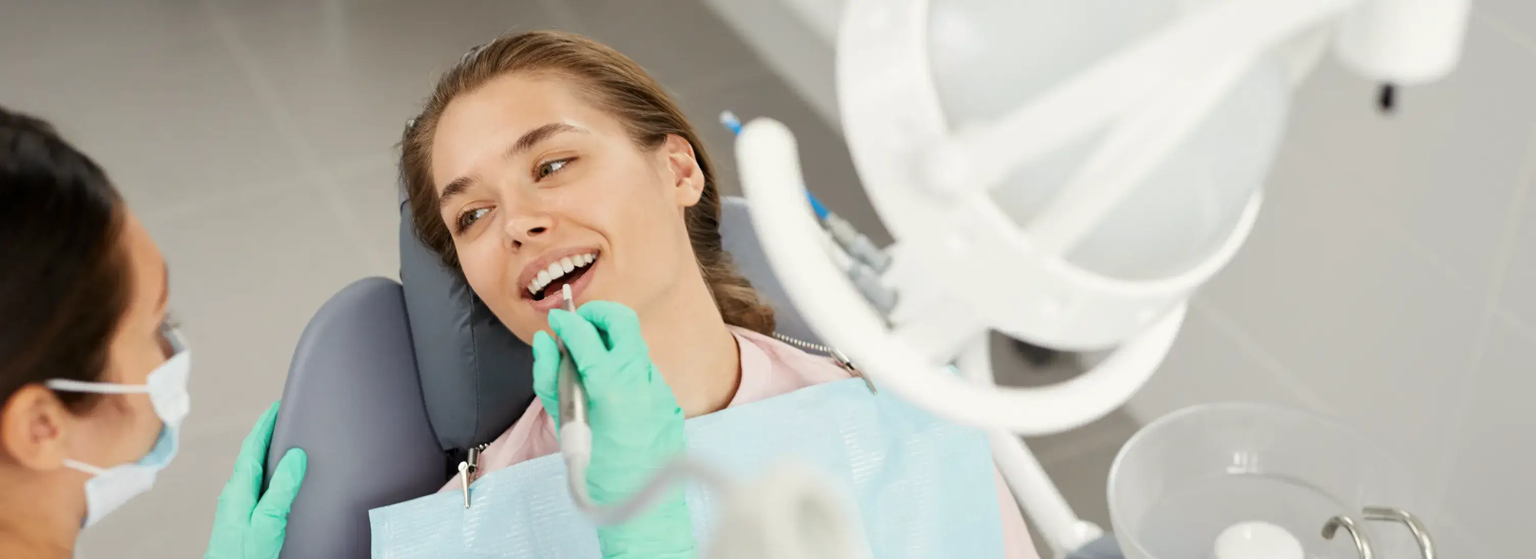 A woman sitting in a dentist chair with a toothbrush in her mouth.