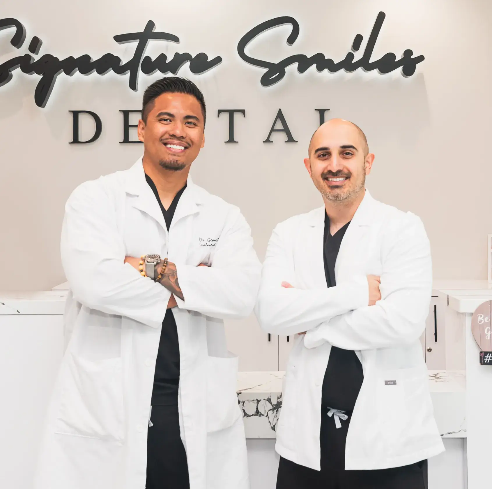 Two men in white lab coats standing in front of a sign.