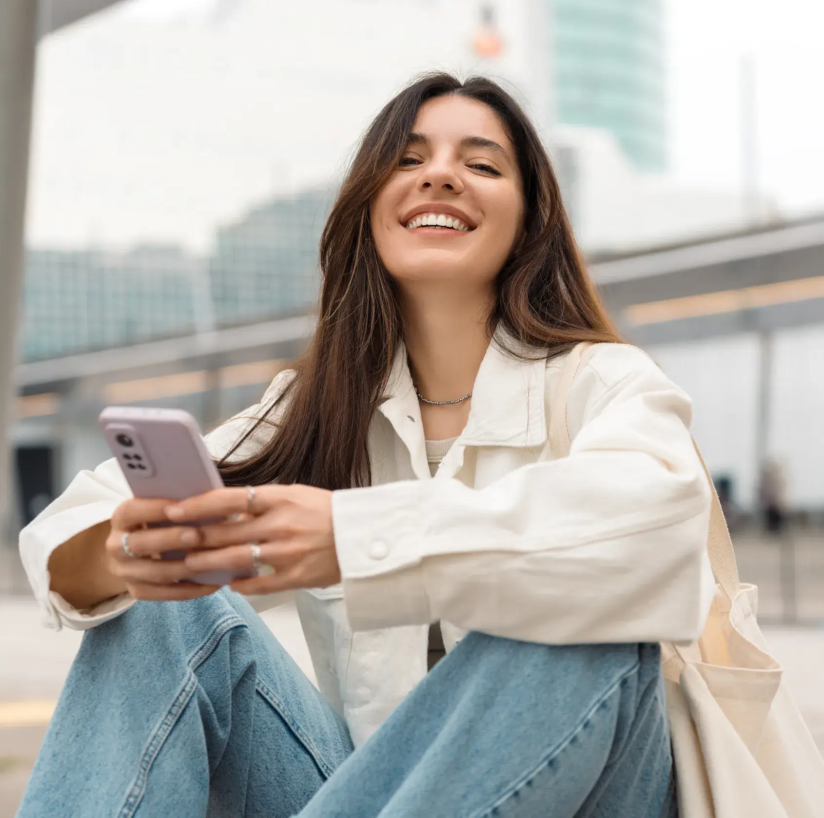 A woman sitting on the ground looking at her cell phone.