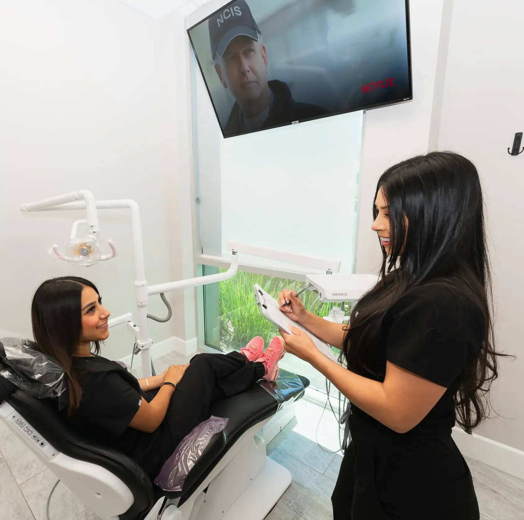 A woman sitting in a dentist chair while another woman holds a toothbrush.
