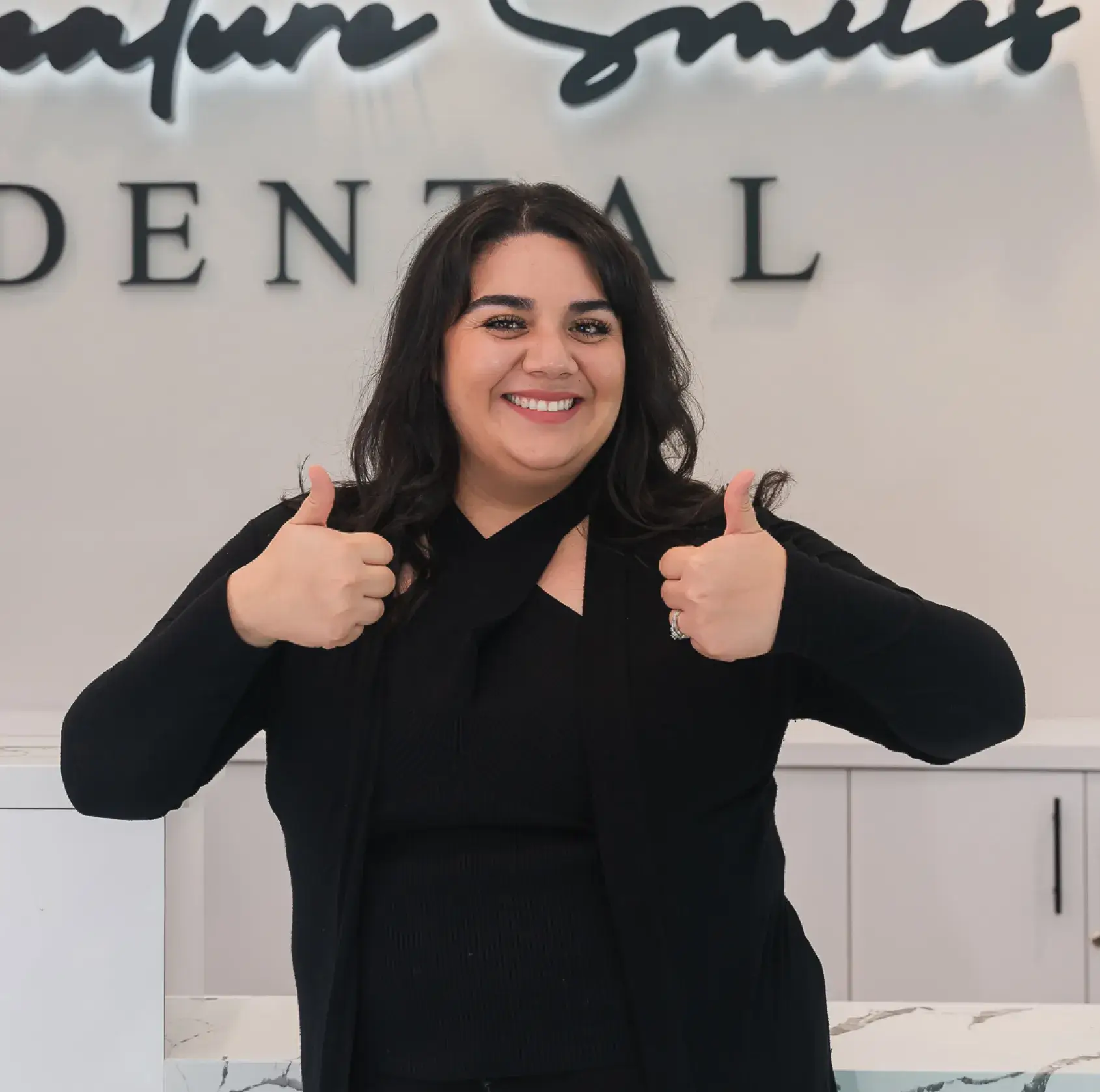A woman giving a thumbs up in front of a dental sign.
