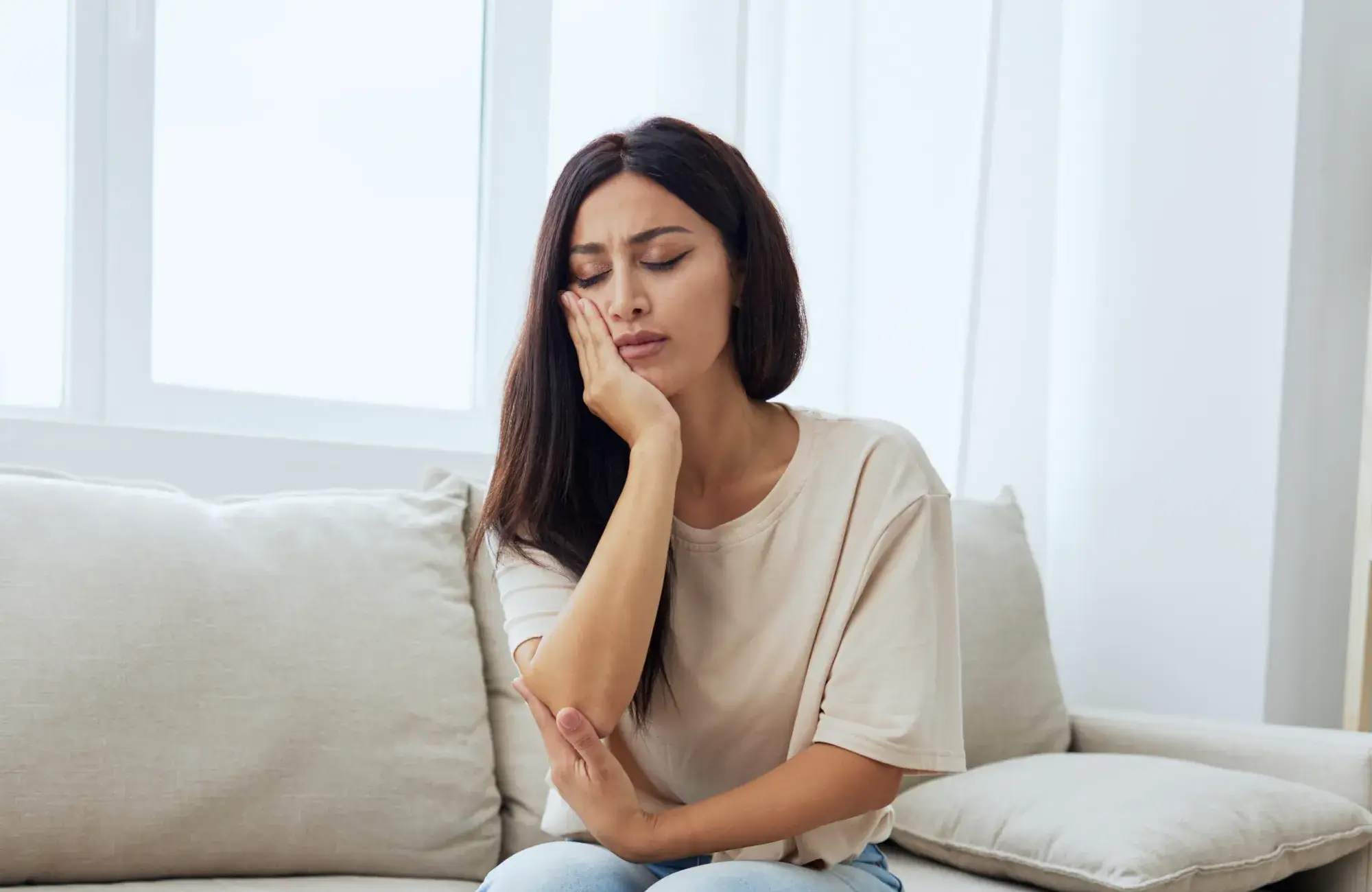 A woman sitting on a couch holding her hand to her face.
