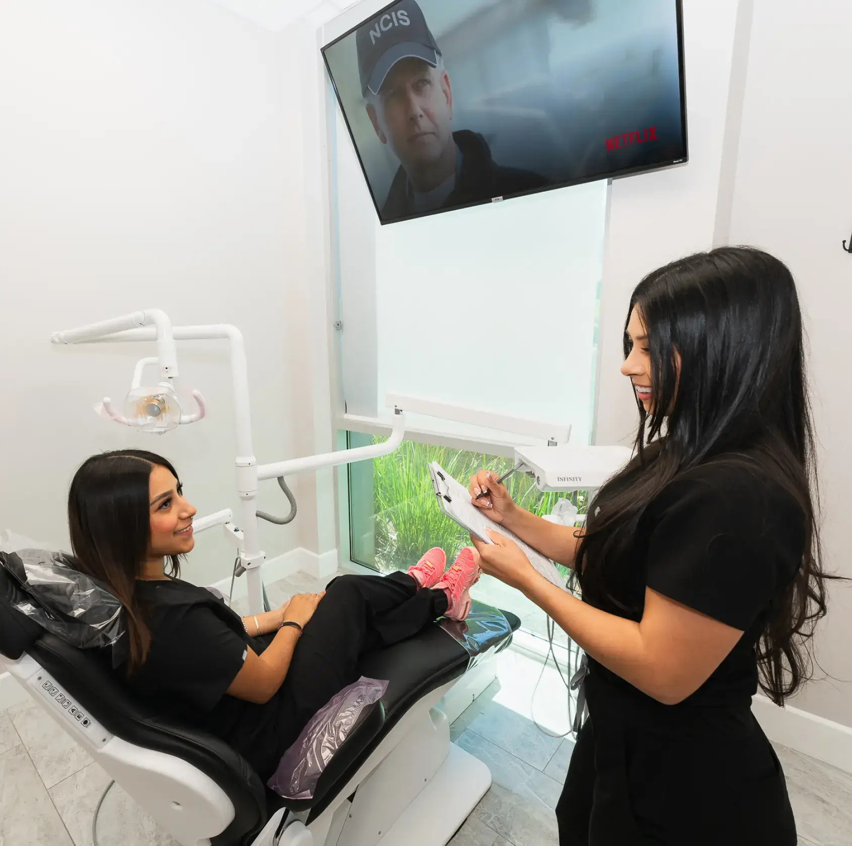 A woman sitting in a dentist chair while another woman holds a toothbrush.