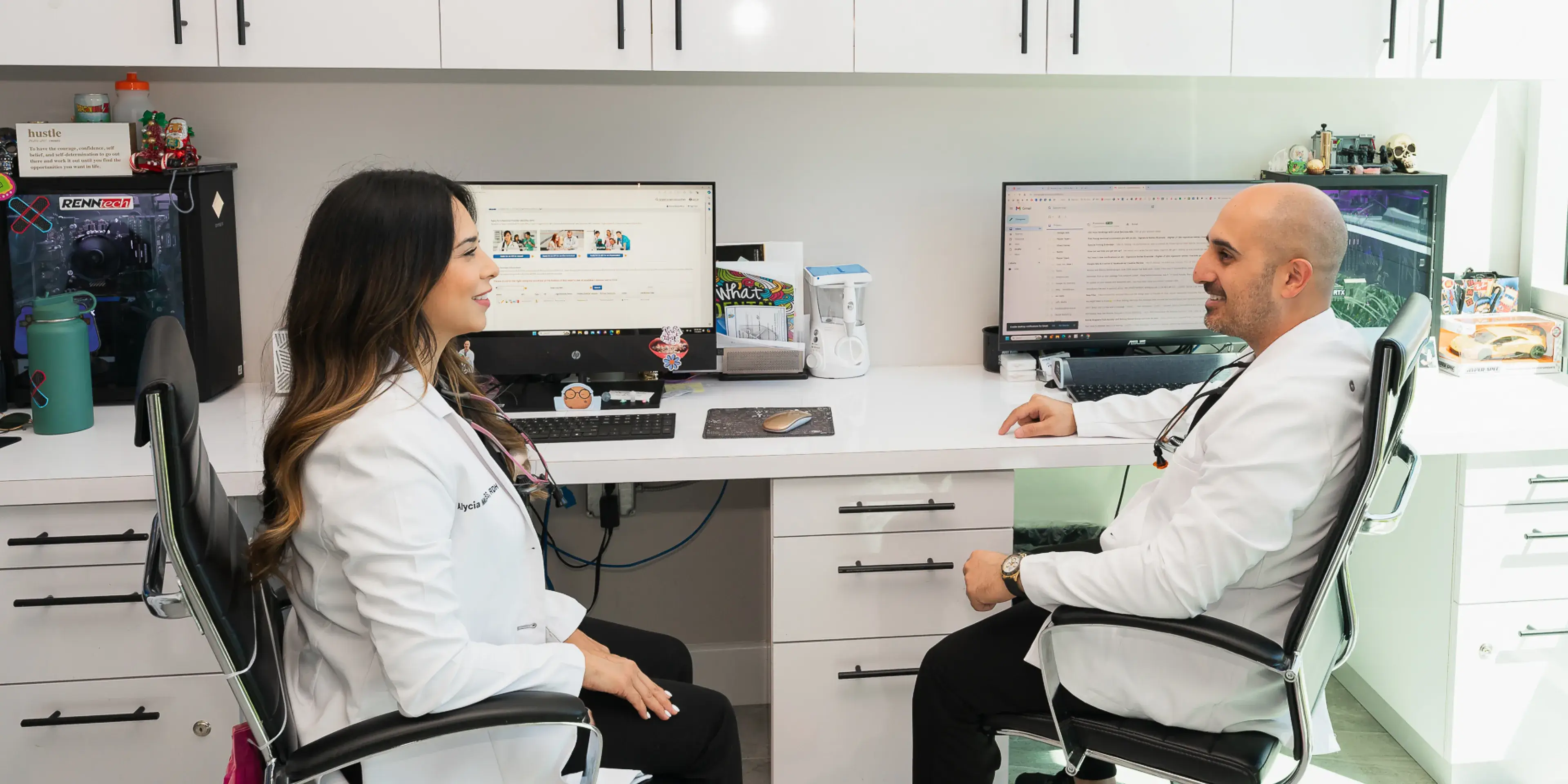 A man and a woman sitting at a desk in front of computer monitors.