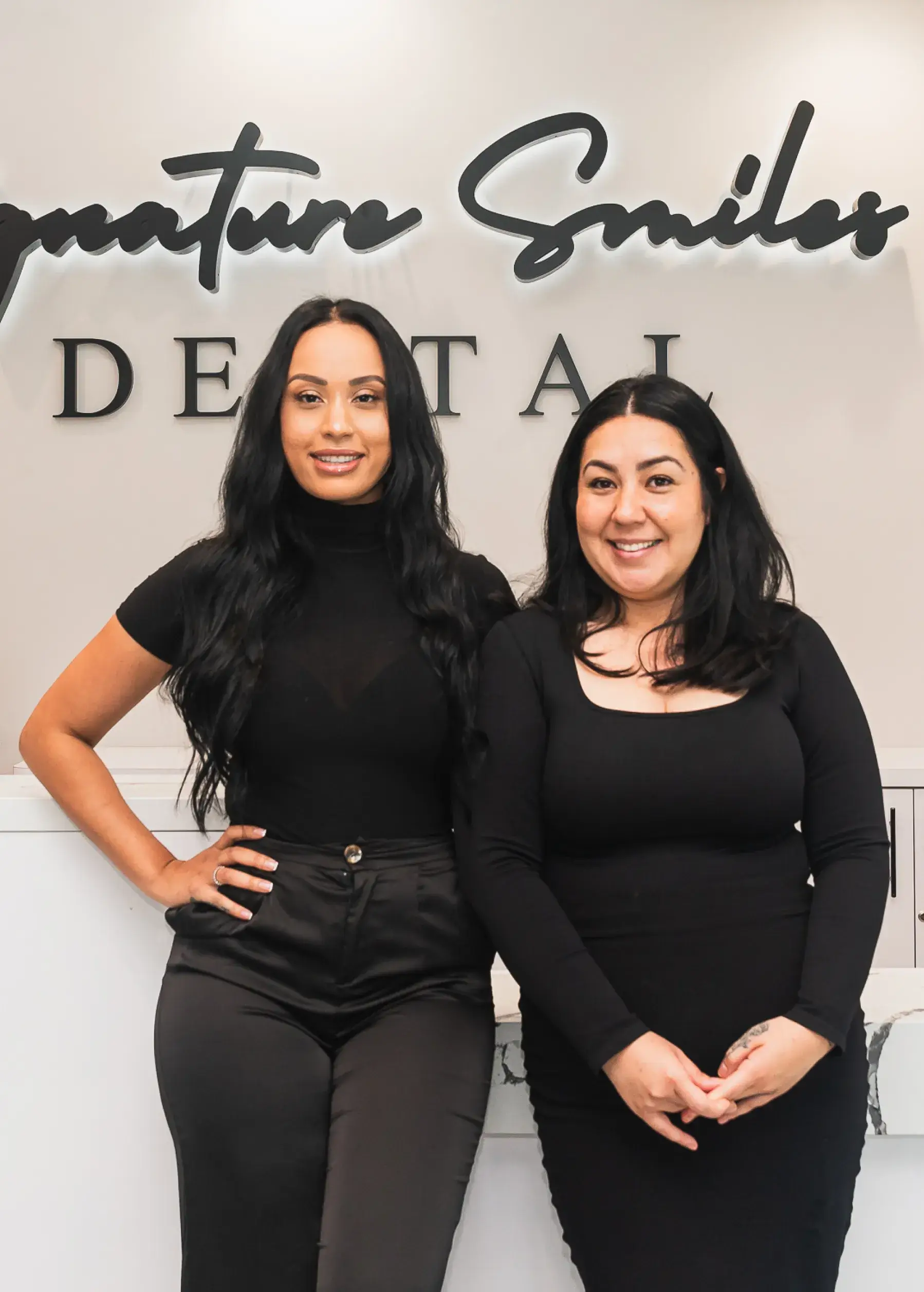Two women standing next to each other in front of a sign.