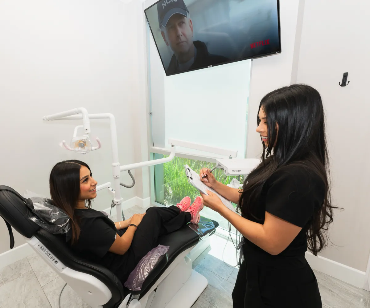 A woman sitting in a chair while another woman holds a toothbrush.