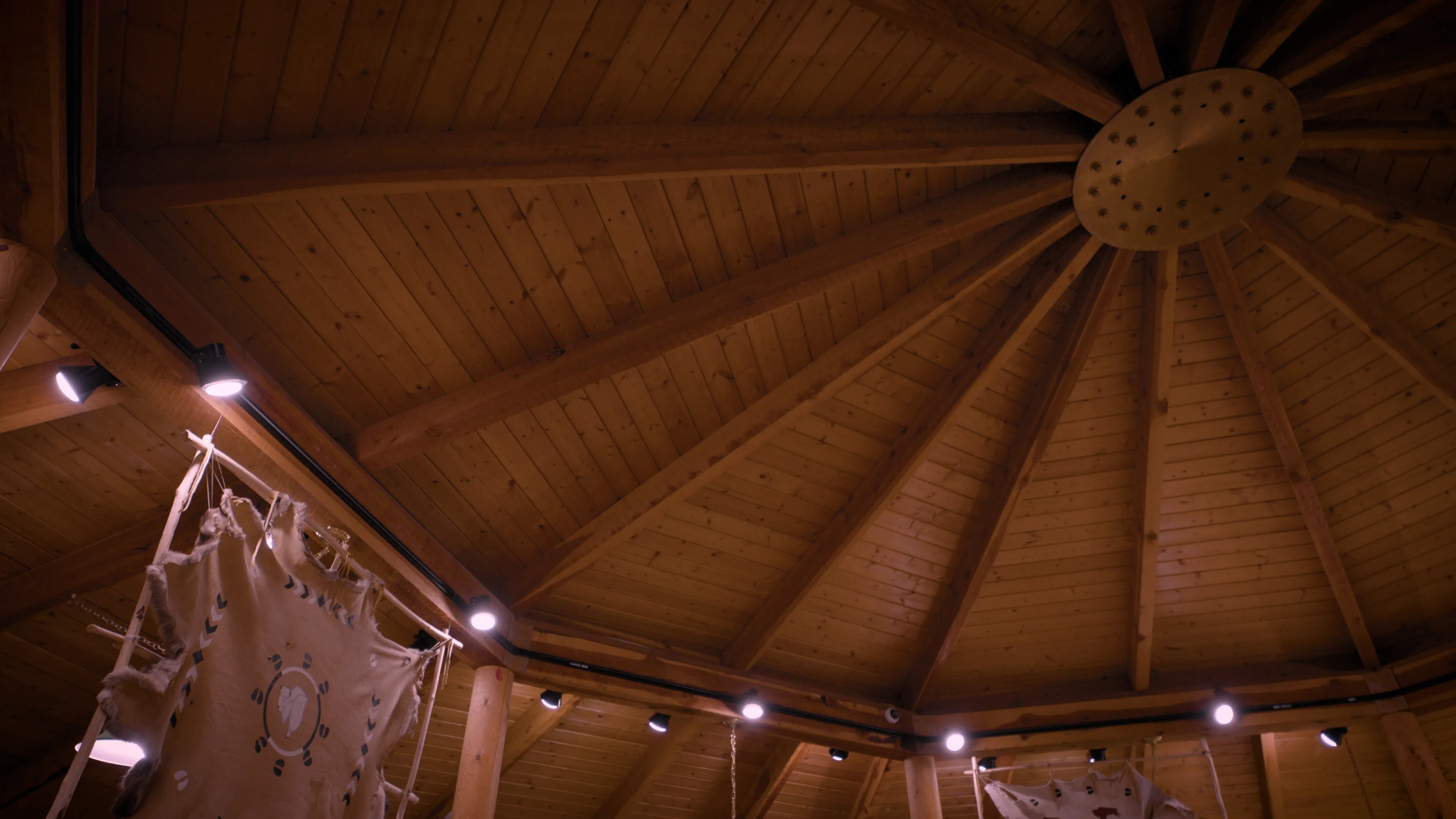 Wooden interior ceiling of a circular structure at Fort Peck Community College, with exposed beams and hanging traditional hide artwork, reflecting Native cultural architecture and design.