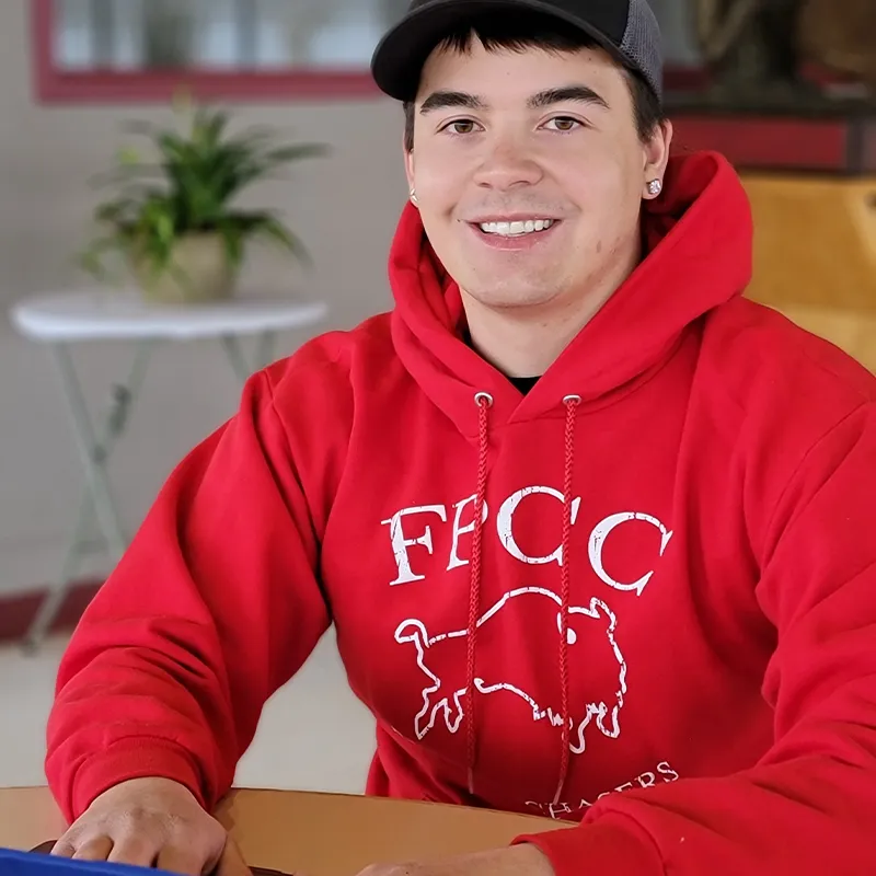 Fort Peck Community College student in an FPCC sweatshirt, smiling confidently while working indoors, representing the start of their college journey.