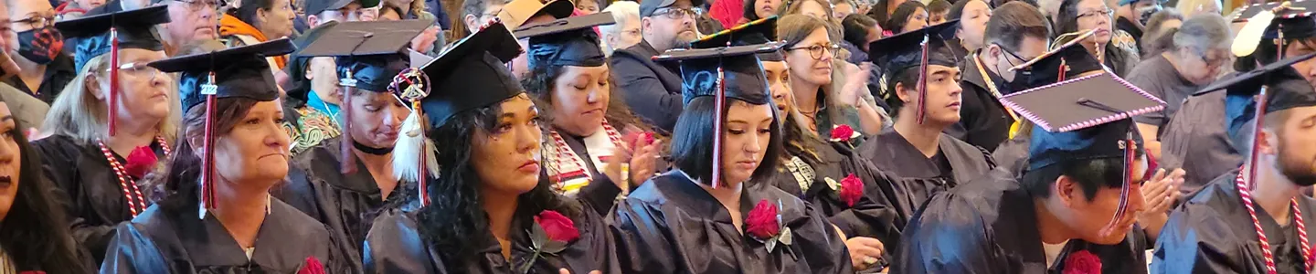 FPCC graduates in caps and gowns seated during a commencement ceremony, many wearing traditional adornments.