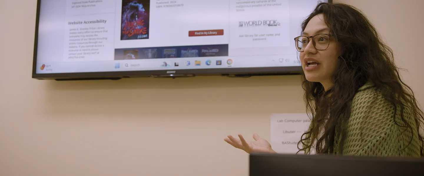 Female instructor speaking in front of a classroom screen showing online learning resources at Fort Peck Community College.
