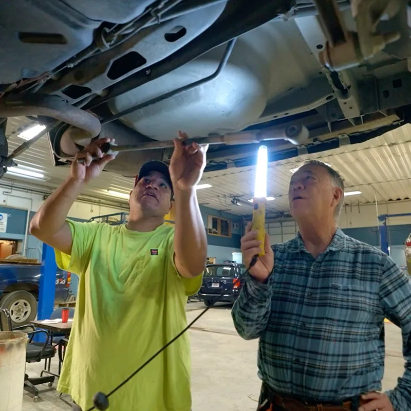 FPCC student and instructor working together under a vehicle in an automotive shop, demonstrating hands-on technical training.