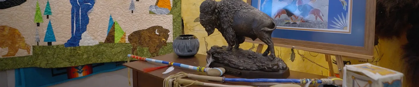 Display of Native artwork and artifacts including a buffalo statue, painted staff, and quilt at Fort Peck Community College, representing tribal history and traditions.