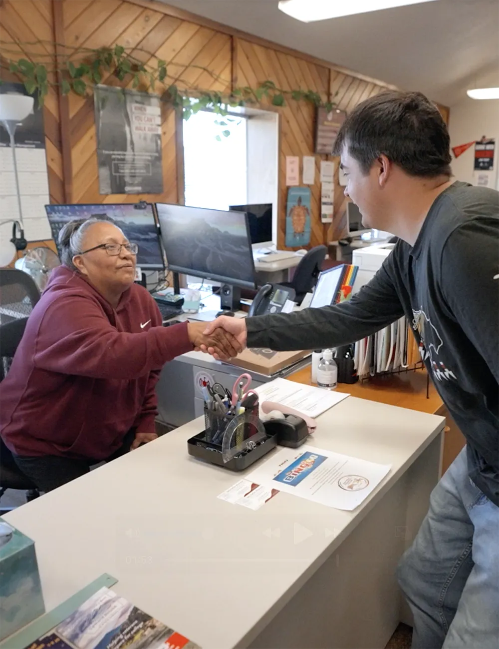 Fort Peck Community College staff member and student shaking hands across a front desk, symbolizing a warm welcome and supportive campus services.