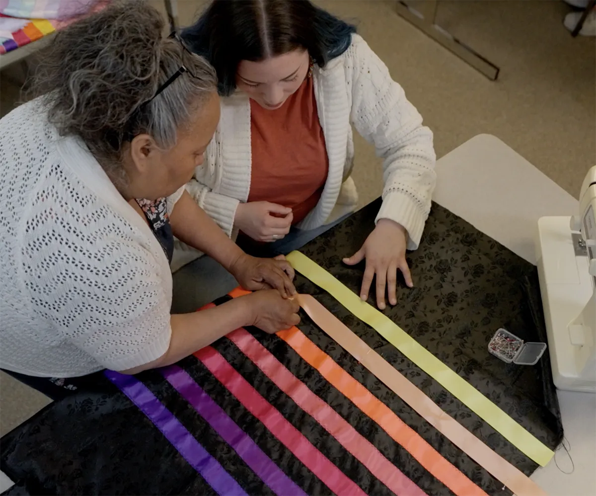 Elder and student at Fort Peck Community College working together on a ribbon skirt project, illustrating intergenerational cultural learning and traditional arts.