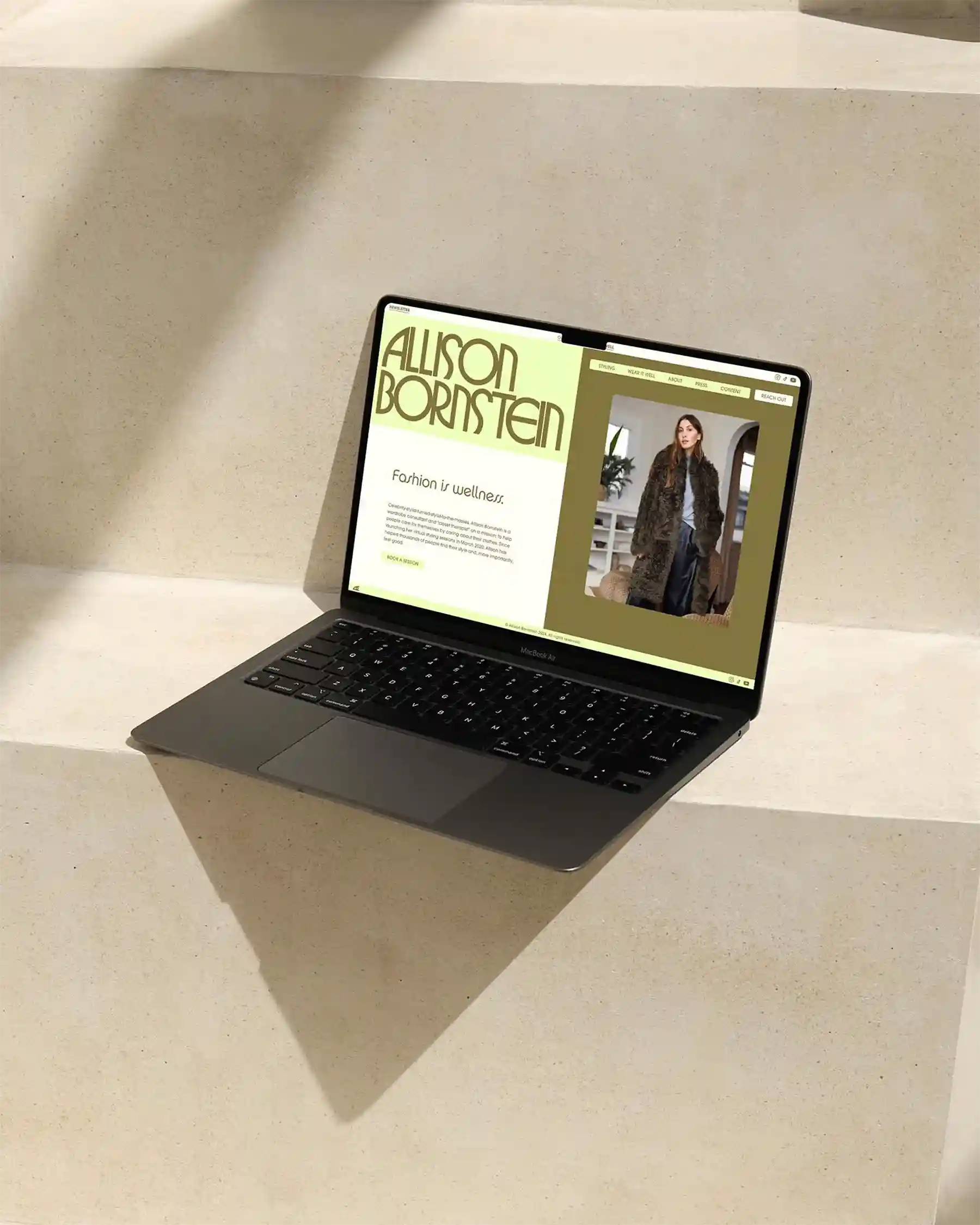 Laptop mockup showing Allison Bornstein website with headline “Fashion is wellness” and woman in fur coat