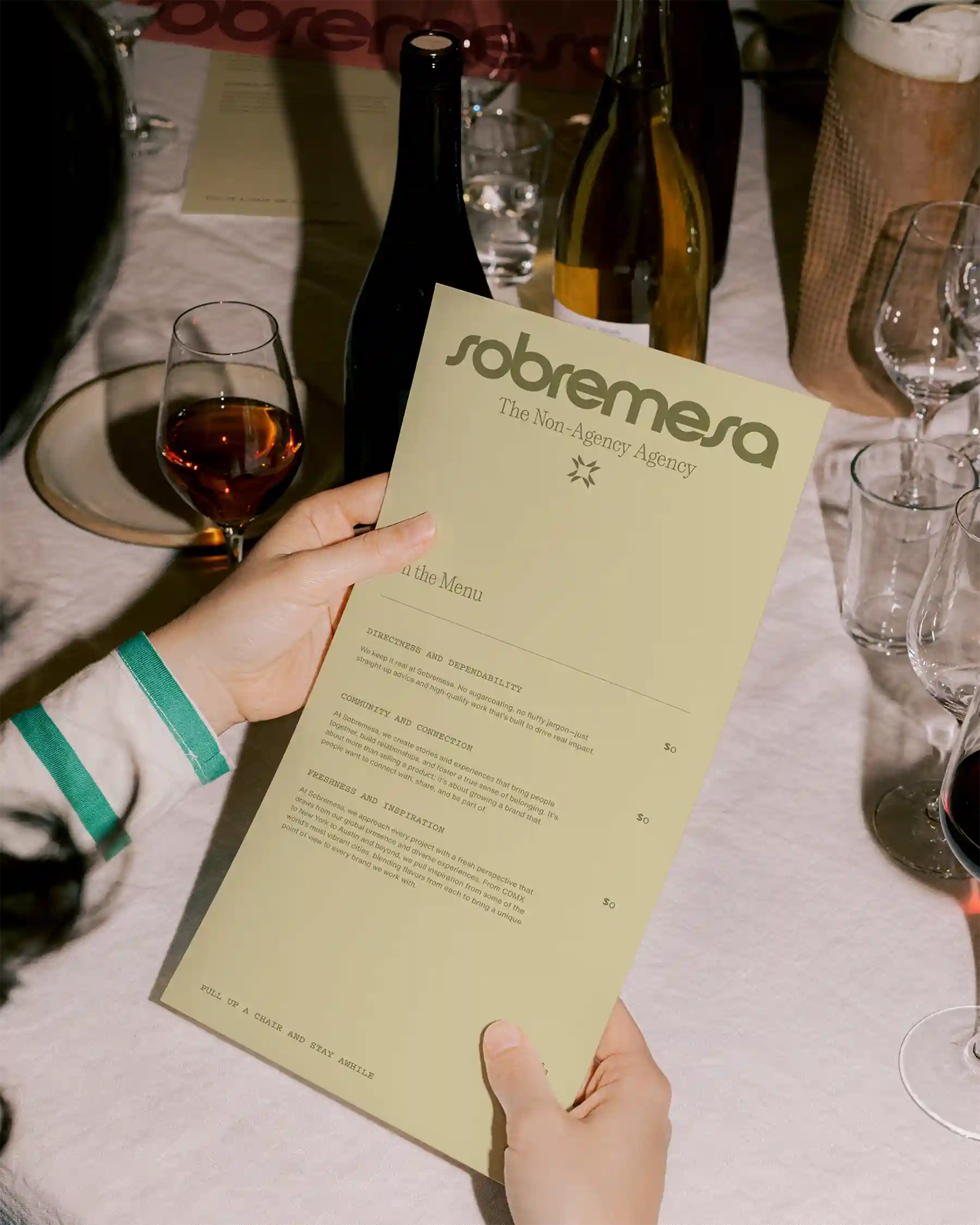 Guest at dinner table holding Sobremesa printed menu with wine and glassware in background