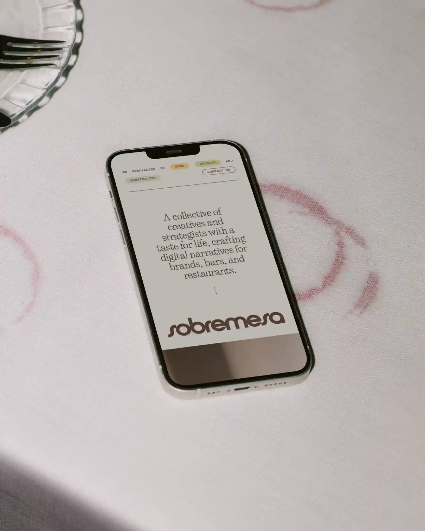Sobremesa website displayed on phone lying on tablecloth with wine glass stains