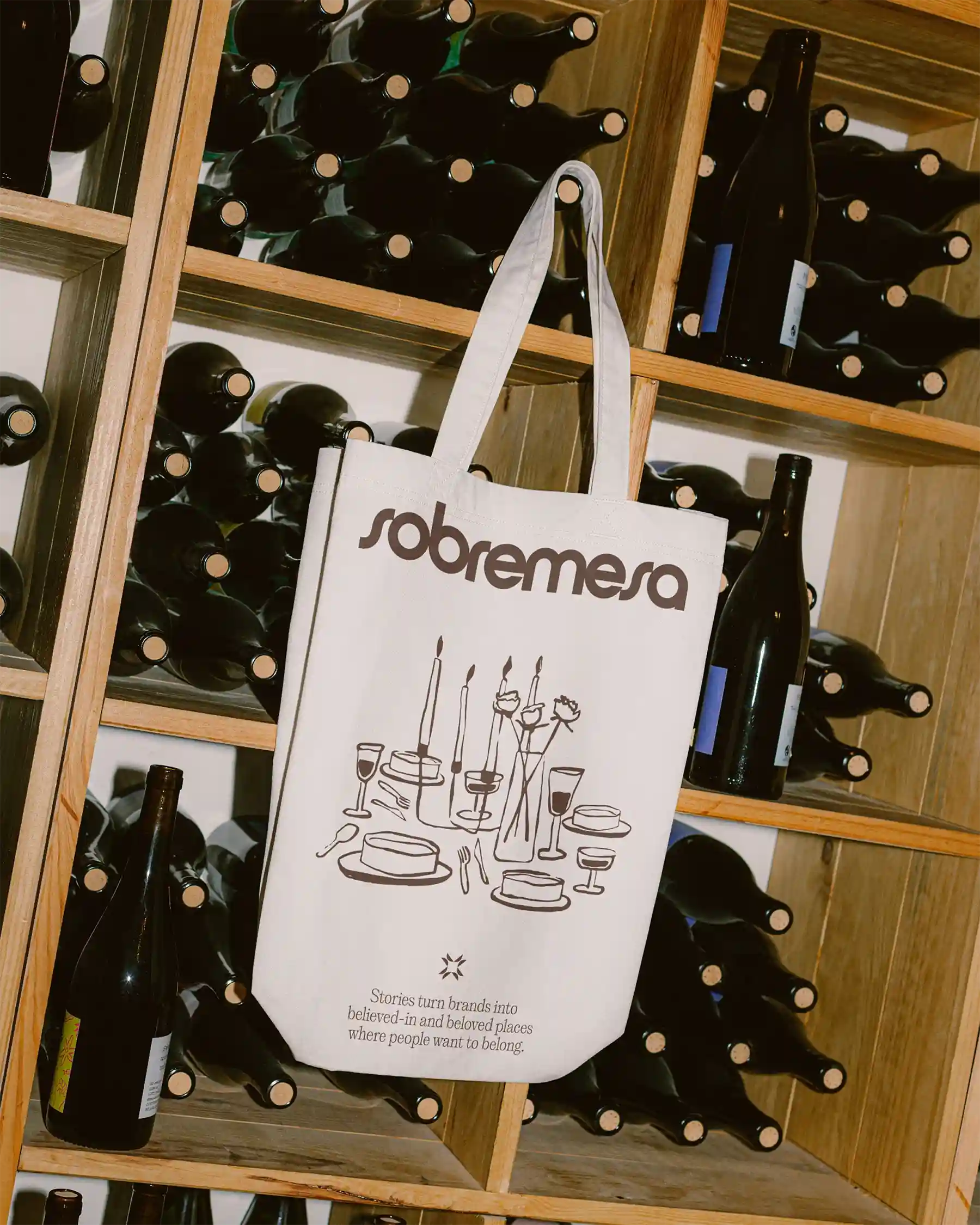 Sobremesa branded tote bag hanging on wine rack surrounded by bottles