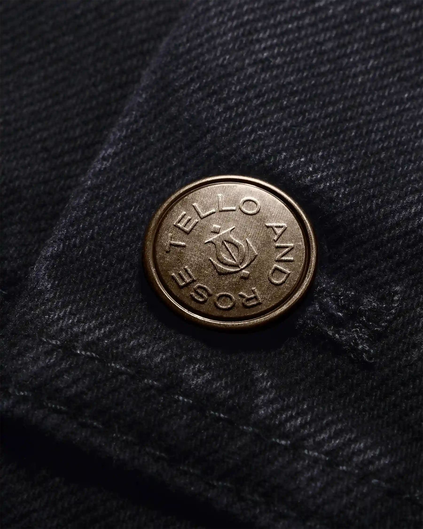 Close-up of copper button engraved with Tello & Rose name on dark fabric