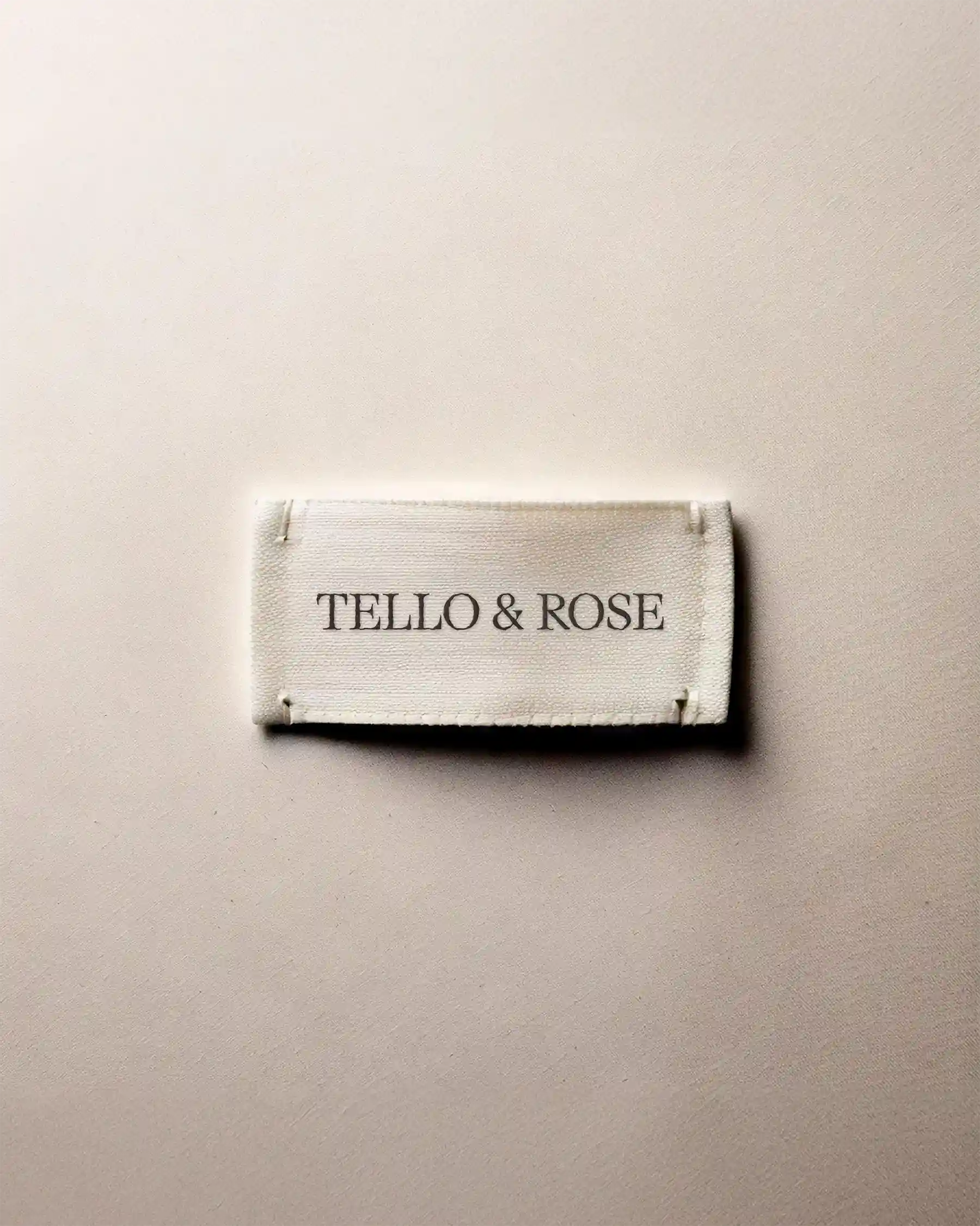 Minimal photo of cream-colored woven clothing label reading “Tello & Rose” on neutral background
