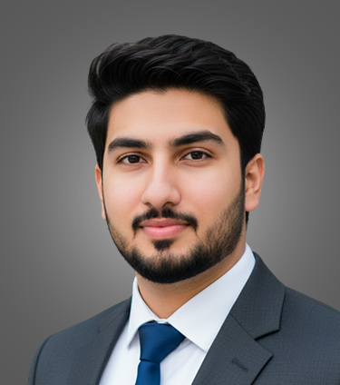 Portrait of a young man with dark hair and beard wearing a gray suit, white shirt, and blue tie against a gray gradient background.