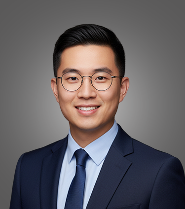 Portrait of a young Asian man wearing round glasses, a blue suit, light blue shirt, and navy tie with a gray background.