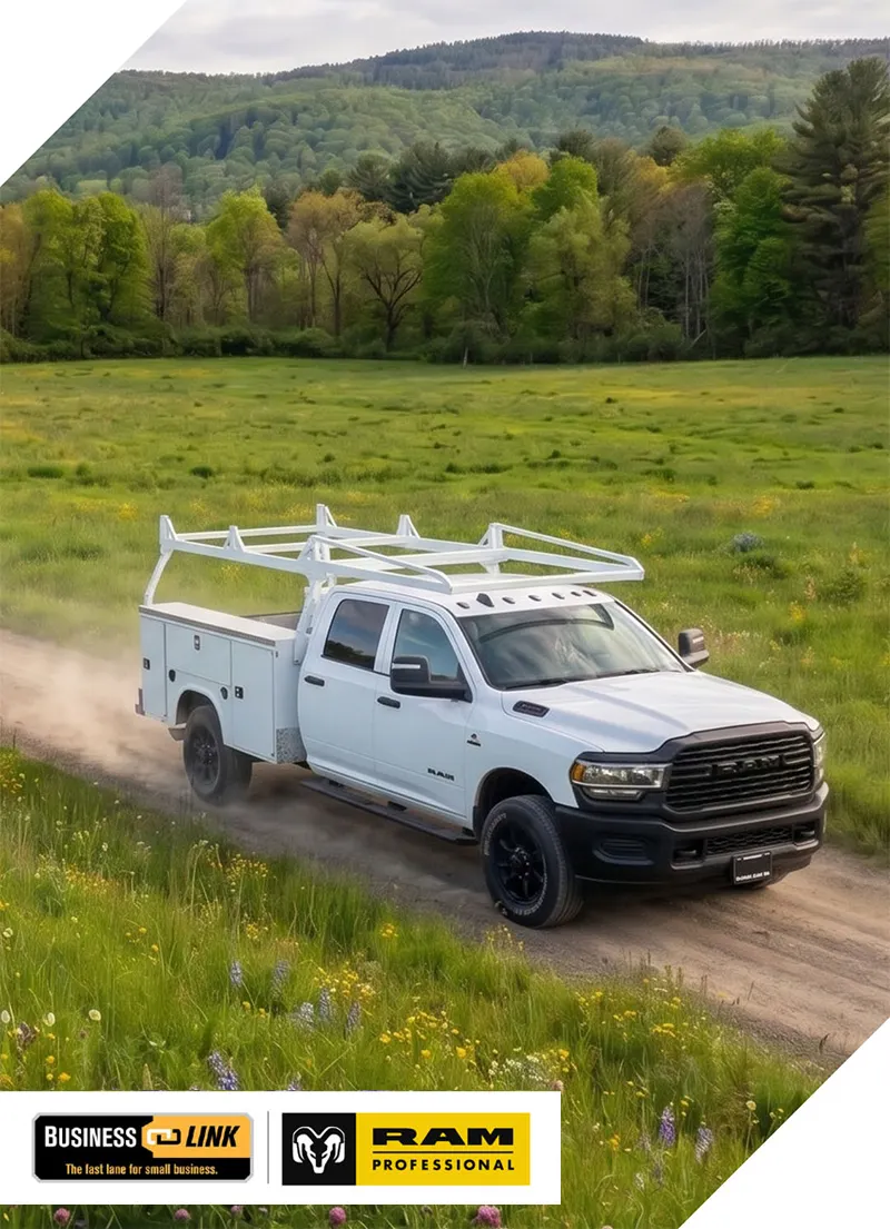 White Ram truck with utility rack driving on a dirt road through a green field with trees and hills.