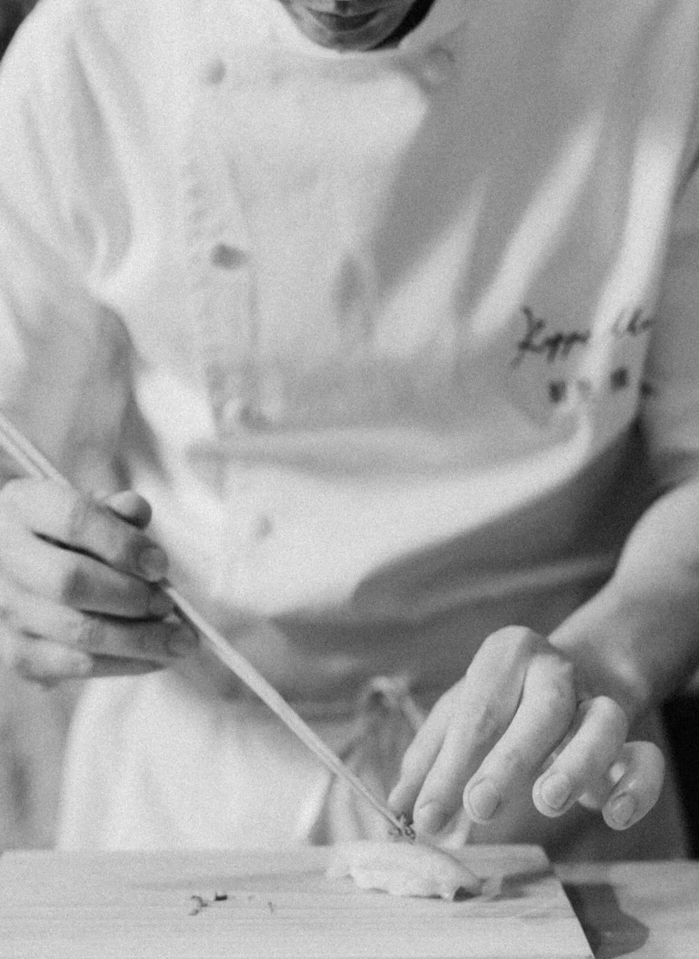 a monotone grainy image of a Chef delicately preparing fish on a wooden counter in the kitchen of the restaurant