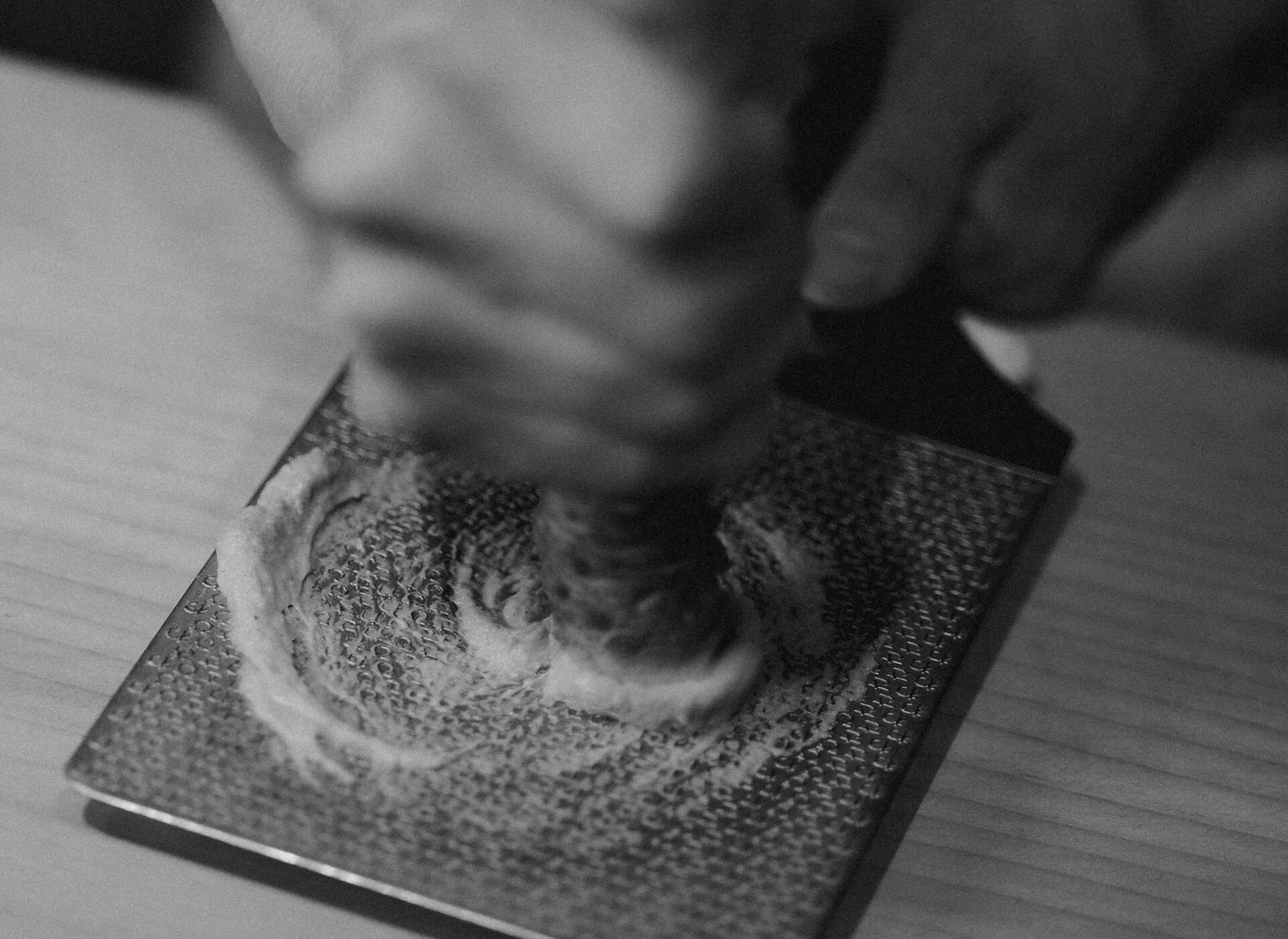 a monotone grainy image of a Chef grating a fresh Wasabi stem.