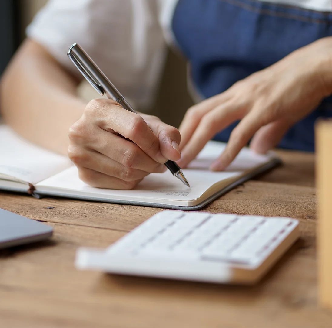 Person writing in a notebook in front of a calculator
