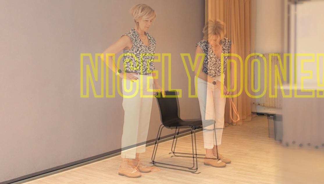 Person standing next to a chair after completing a seated movement exercise, with the words ‘Nicely Done!’ displayed across the image