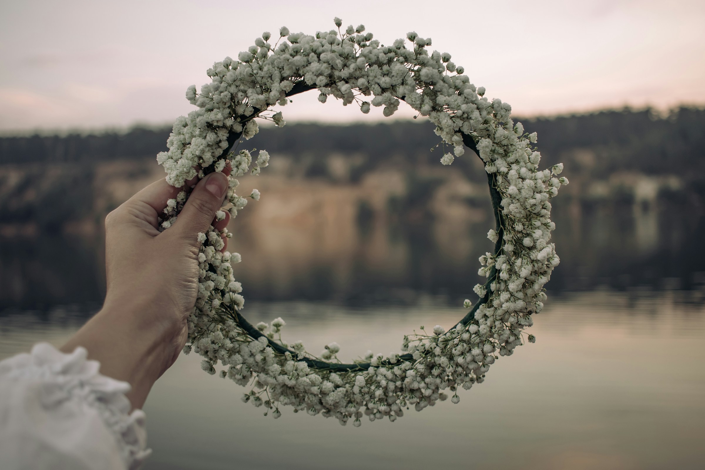 Close-up of a circular floral wedding arch made of white baby’s breath flowers by the water — elegant outdoor wedding decor captured in soft natural light.