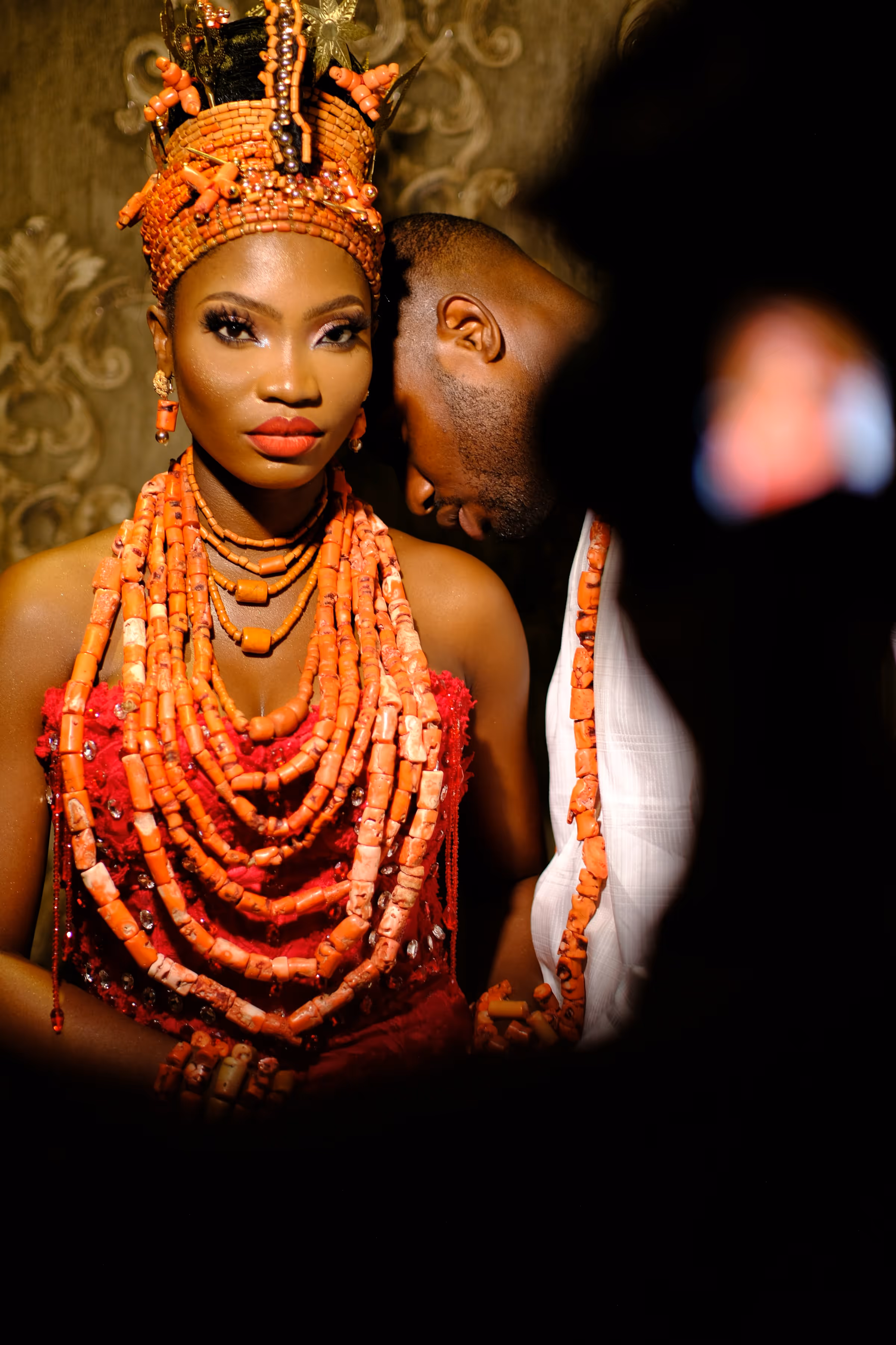 Bride wearing traditional red coral beads and embracing groom — intimate cultural wedding moment highlighting love and heritage.