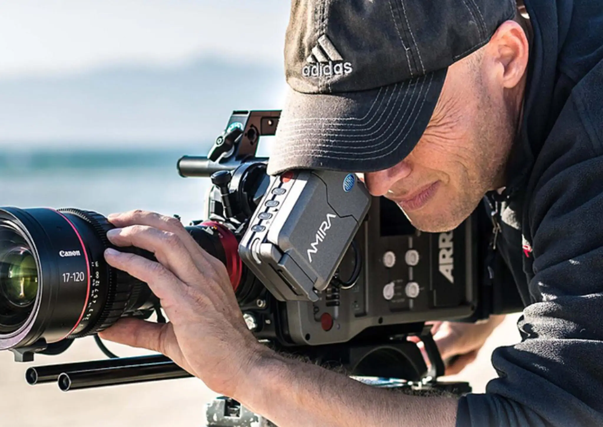Man wearing Adidas cap adjusting the lens on a professional ARRI Mira video camera outdoors.