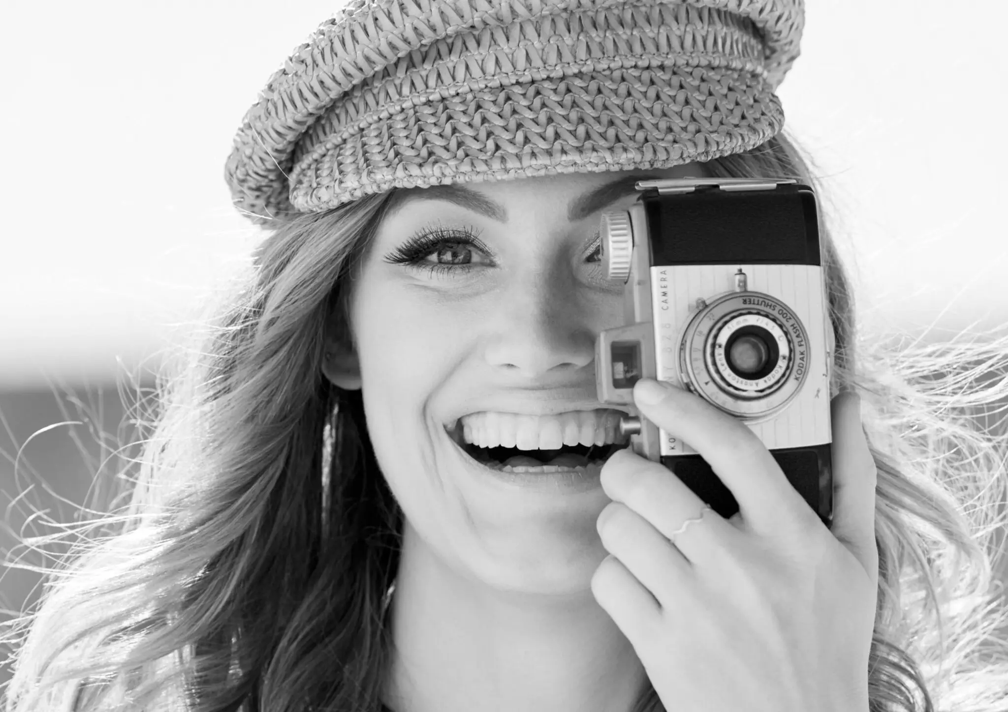 Woman smiling while holding a vintage Kodak camera up to her eye.