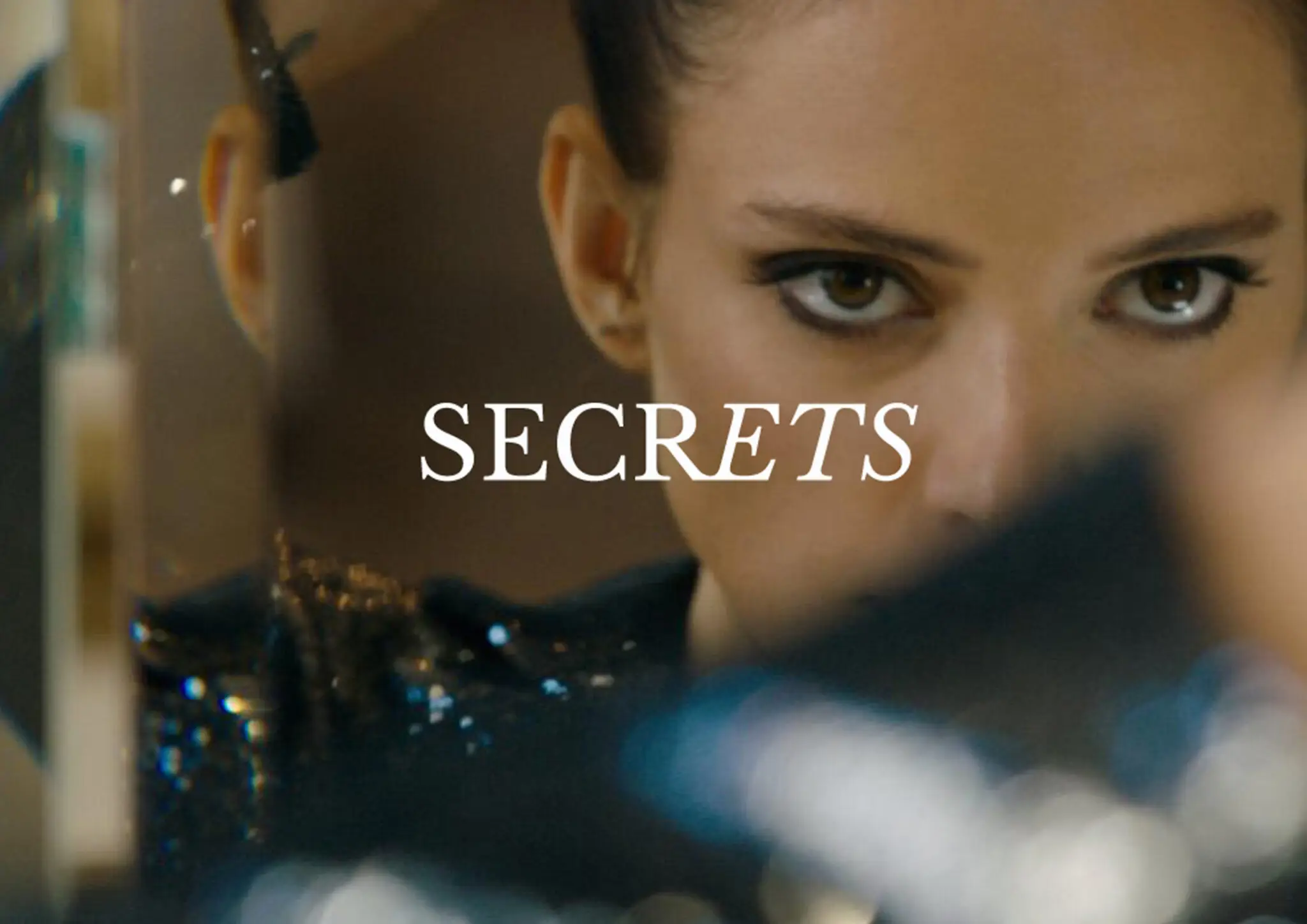 Close-up of a woman looking into a mirror with the word SECRETS overlaid.