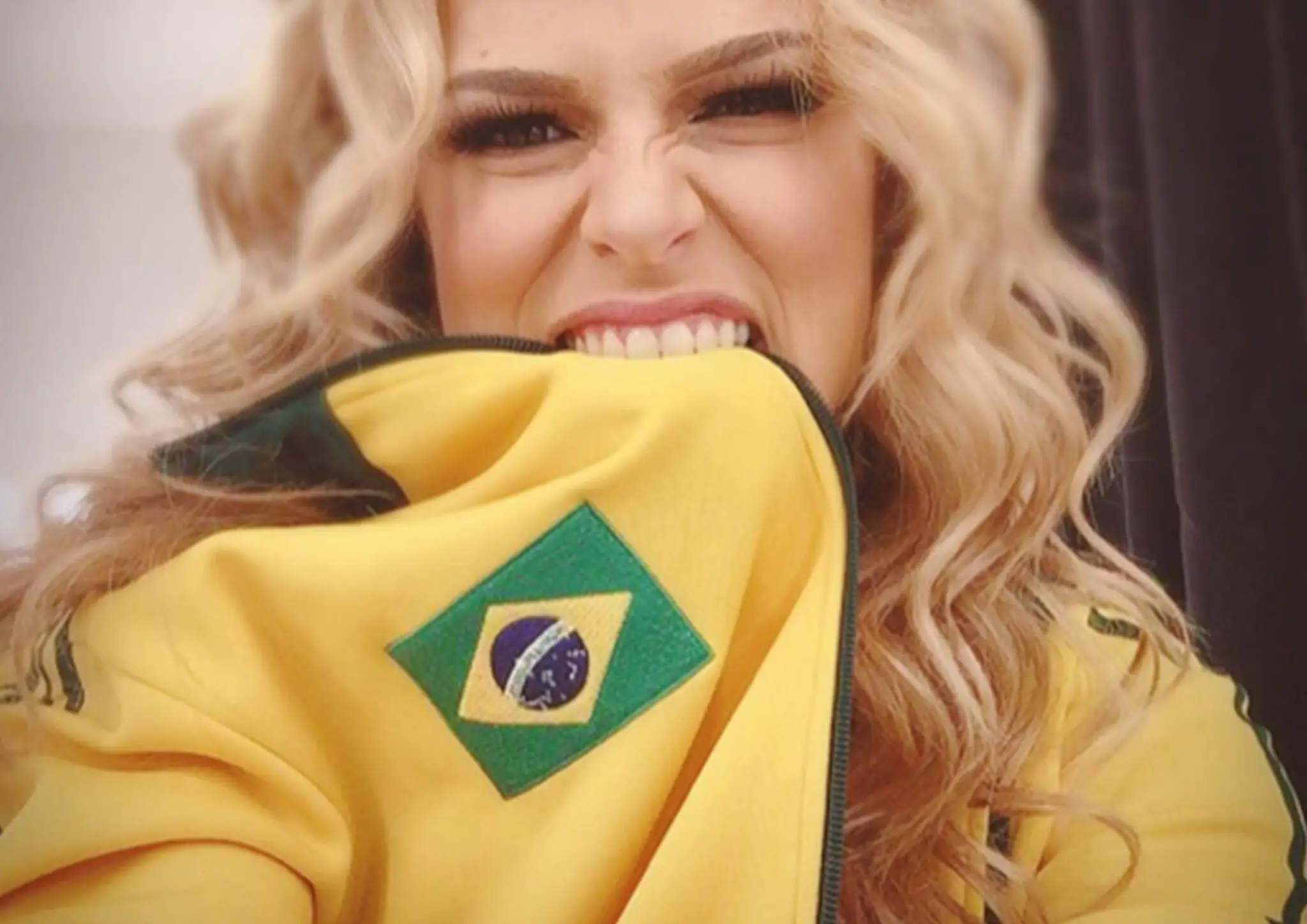 Ferly biting the collar of a yellow jacket featuring the Brazilian flag emblem.