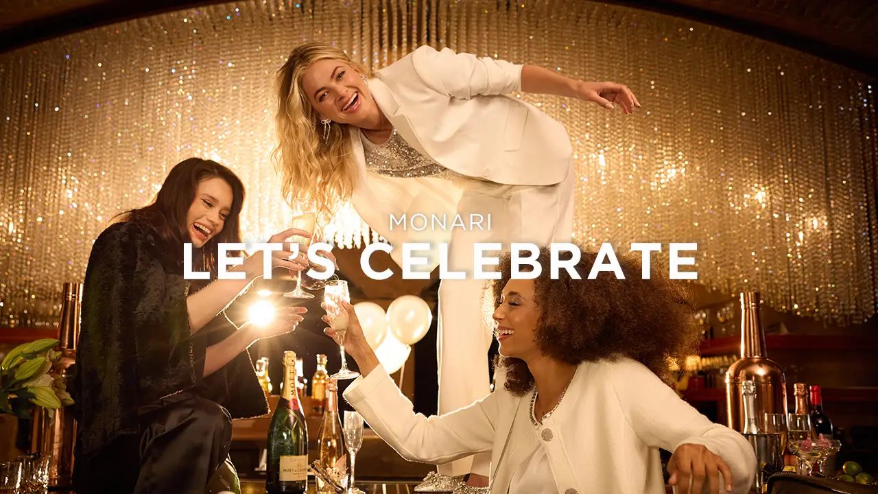 Three joyful women toasting with champagne glasses in a festive setting with golden decorations and bottles.