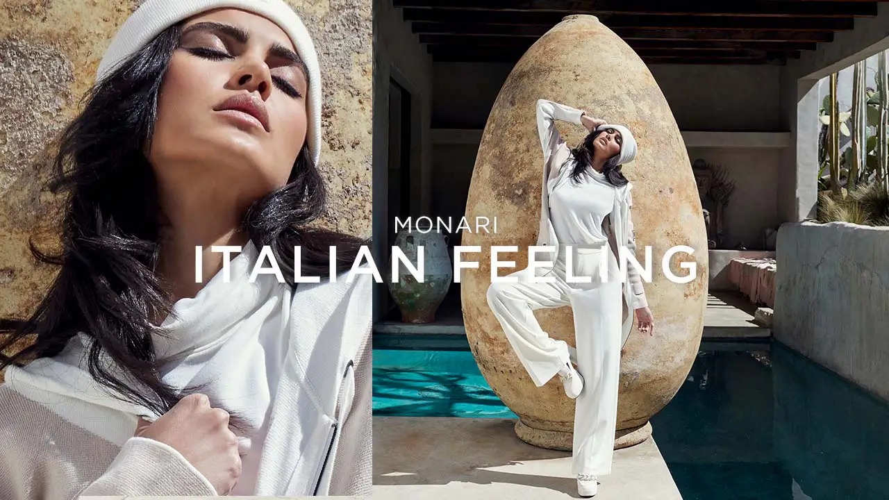 Fashion model wearing white outfit and beret posing outdoors by a large stone sculpture and pool.