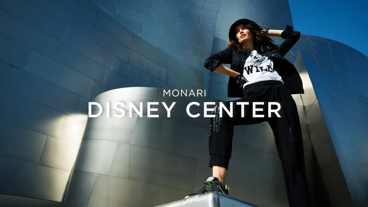 Fashionable woman in black outfit posing confidently against curving metallic building under clear blue sky.