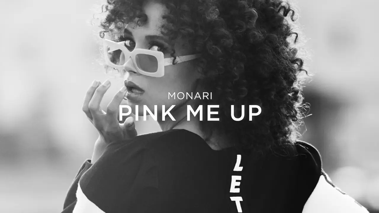 Woman with curly hair wearing large square sunglasses and a black top, looking over her shoulder.