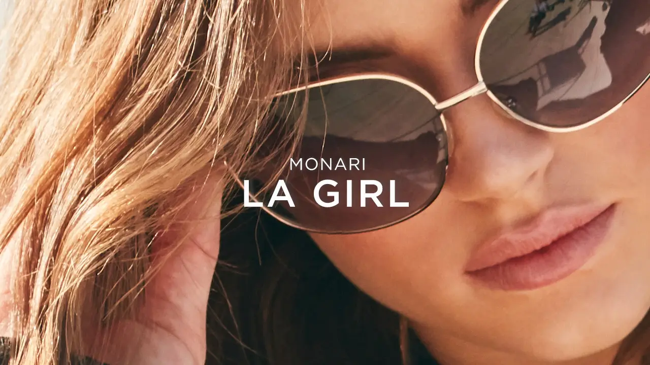 Close-up of a woman wearing large reflective sunglasses with text 'MONARI LA GIRL' overlayed.