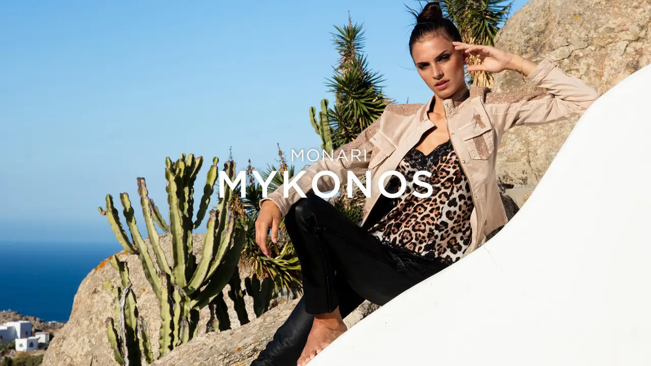 Woman in beige jacket and leopard print top posing on a rock with cacti and blue sky in the background.