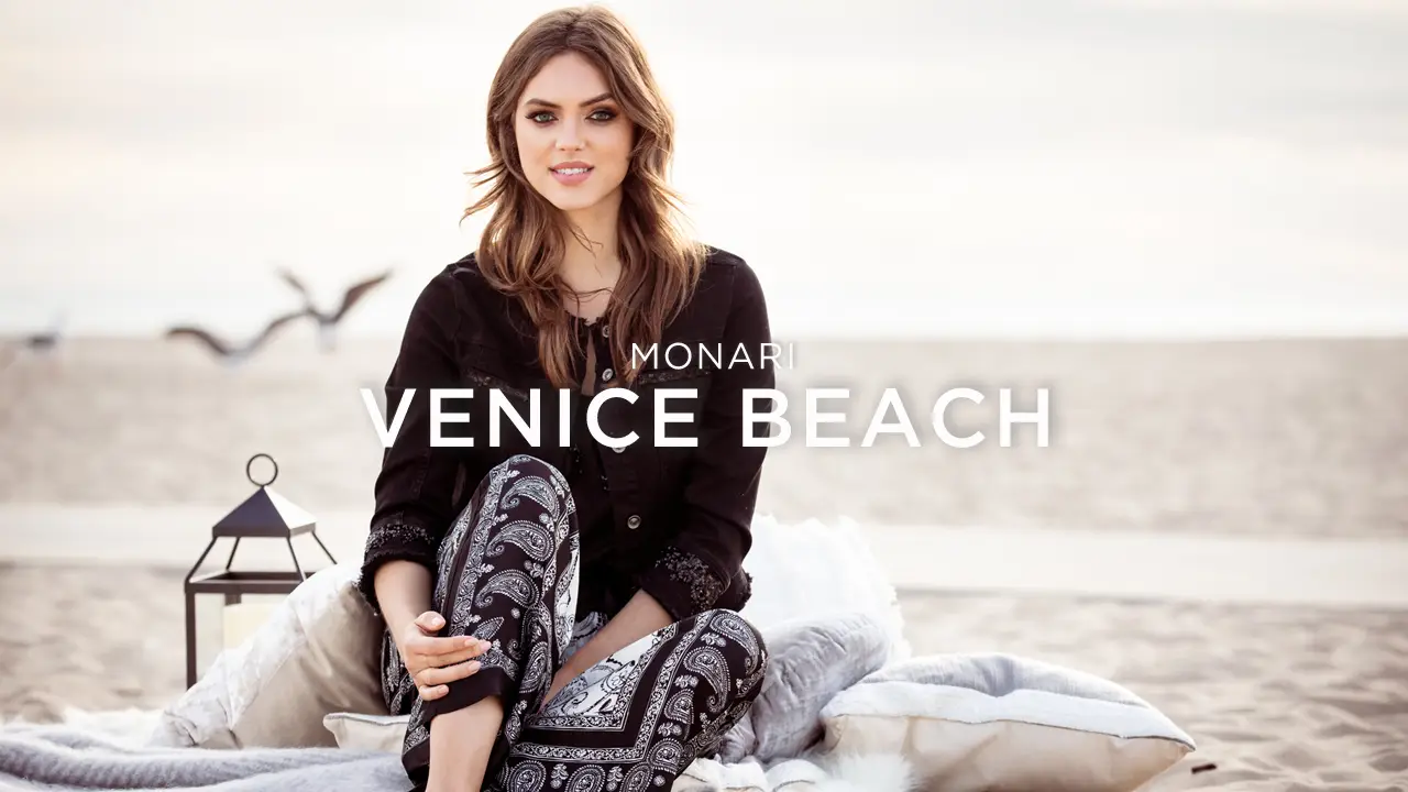Smiling woman sitting on blankets on a sandy beach with a lantern nearby and text 'Monari Venice Beach.'