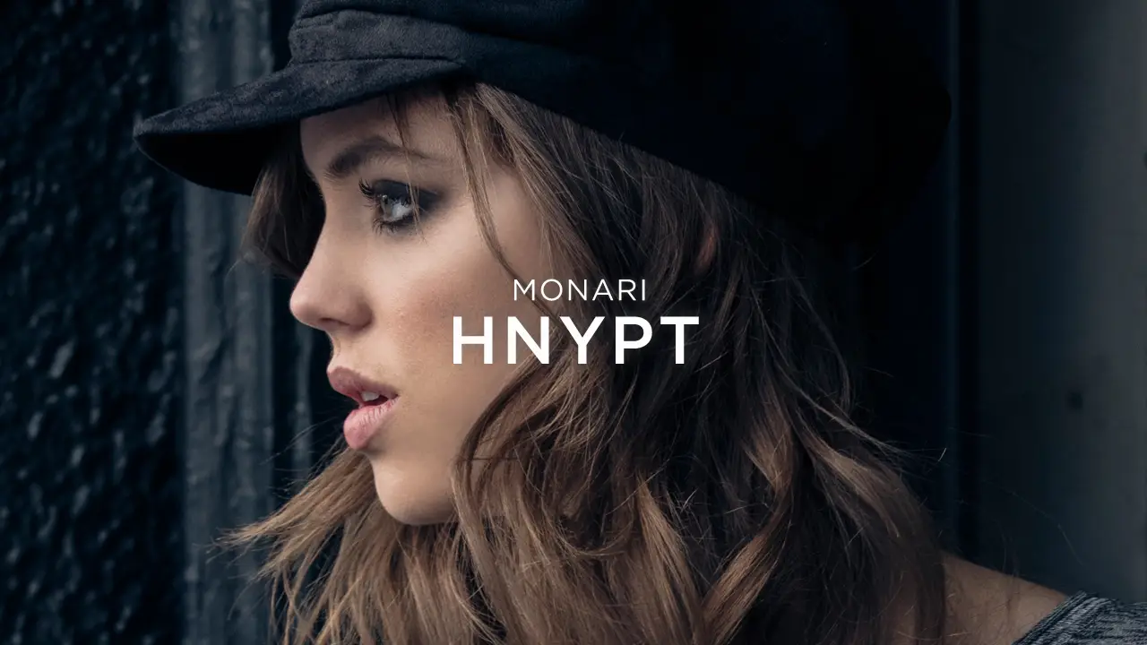 Side profile of a woman with wavy hair wearing a black cap next to a textured dark surface.