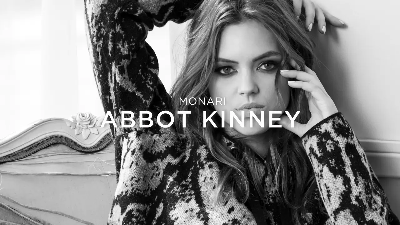 Black and white portrait of a woman with long hair wearing a patterned sweater, posing with one arm behind her head and the other touching her face.