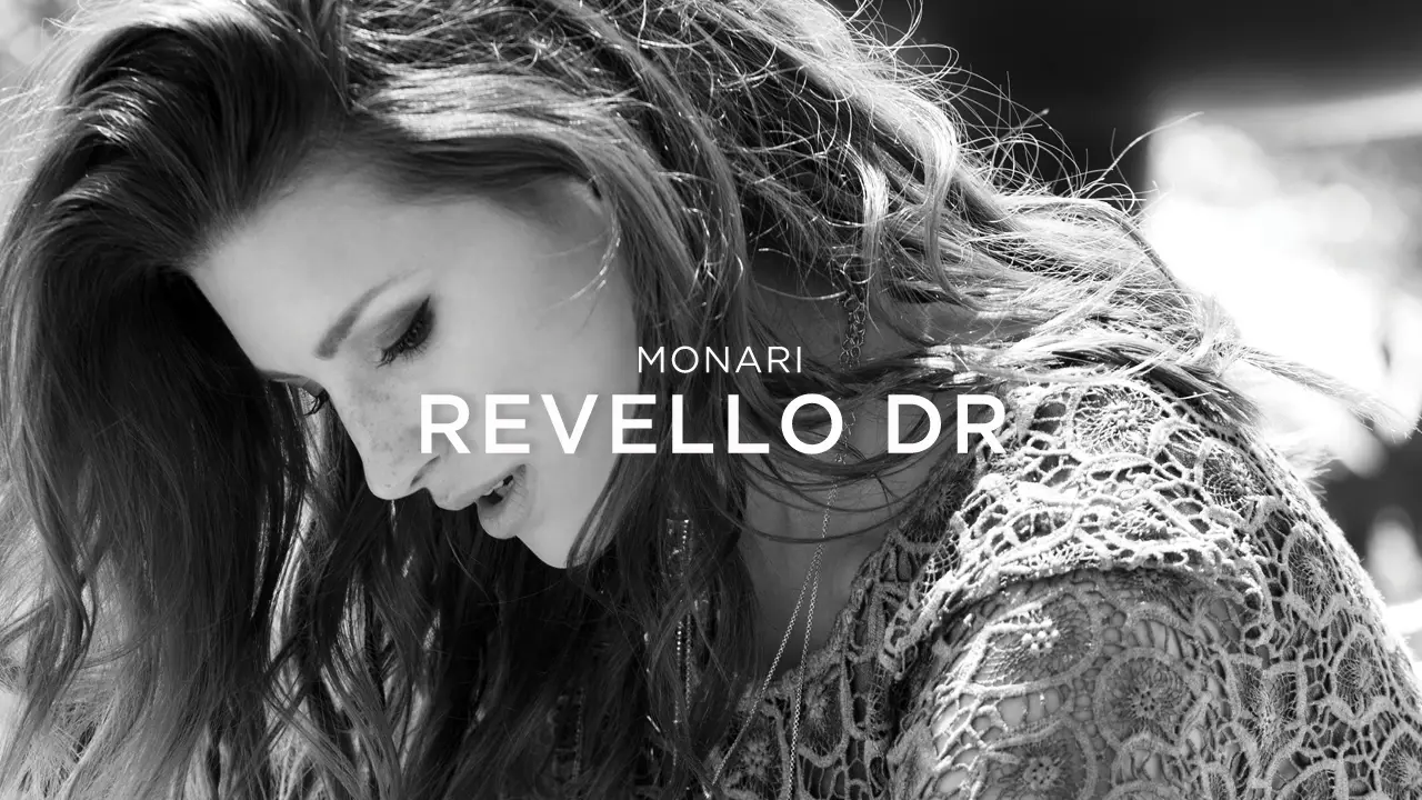 Black and white close-up of a woman with long wavy hair wearing a lace garment, with text overlay 'Monari Revello Dr'.